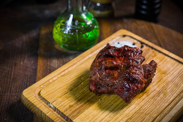 Grilled pork rib chop steak in a clay plate with oil, mustard, salt and rosemary is an old wooden table.