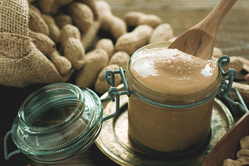 Organic Peanut Butter in Glass Jar with Peanuts in Shell on Wooden Background. Healthy Breakfast Vegetarian Food Concept.