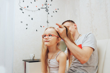 young father combs his little daughter while they spend time together at home