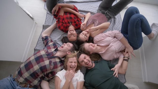 friends tickle each other while lying on their backs and laughing merrily at the camera during a home party