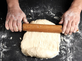 chef in a black tunic rolls a dough for a round pizza