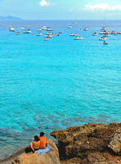 Fototapeta premium people inside paradise clear torquoise blue water with boats and cloudy blue sky in background in Favignana island, Cala Rossa Beach, Sicily South Italy.