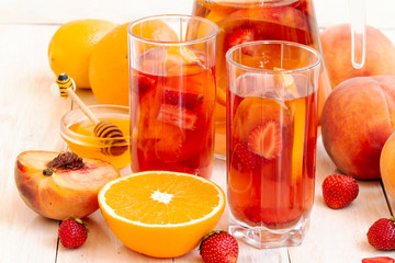 Summer refreshing drinks. Fruit, berry cocktail. compote with peach, strawberry, orange, hioney. Cold fruit and berry tea in faceted highball, healthy drink. Dietary detox drink on light background.