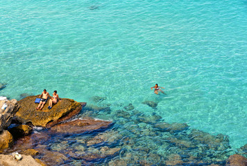 Fototapeta na wymiar people inside paradise clear torquoise blue water with boats and cloudy blue sky in background in Favignana island, Cala Rossa Beach, Sicily South Italy.