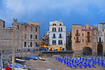 the beach in front of the port of Cefalù with old buildings and architecture on summer evening with cloudy sky, sicily Italy