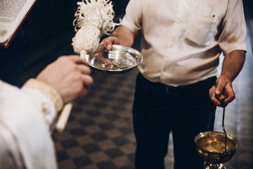priest blessing golden wedding rings on plate in church before wedding ceremony, religion traditions.