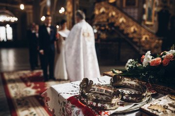golden crowns on altar and priest putting on golden wedding rings on couple hand in church wedding...