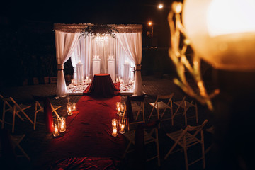 wedding evening decor for ceremony, venue aisle with candles in glass lanterns and arch, stylish...