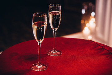 glasses with bubble champagne on red table at evening wedding ceremony reception, with lights in garden. space for text. romantic moment for wedding couple