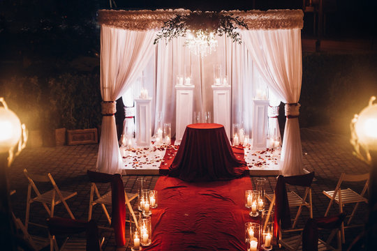 Wedding Evening Decor For Ceremony, Venue Aisle With Candles In Glass Lanterns And Arch, Stylish Wedding Decoration For Night Ceremony In Garden, Lights. Beautiful Romantic Place