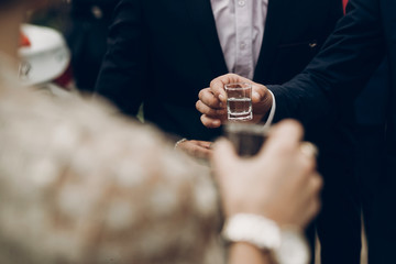 people holding glasses of vodka and toasting at wedding reception, celebration outdoors, catering in restaurant. christmas and new year - obrazy, fototapety, plakaty