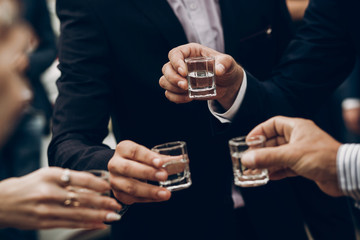 people toasting holding glasses of vodka cheering at wedding reception, celebration outdoors, catering in restaurant. christmas and new year - obrazy, fototapety, plakaty