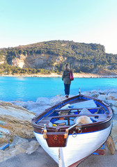 Portovenere, Italy  View on Palmaria island from Portovenere beach with young woman on the rocks and old  wooden boat . Liguria