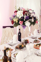beautiful rustic bouquets flowers in vases at wedding tables with food in restaurant, luxury wedding reception, stylish decor and catering.