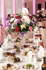 flowers in vases and numbers of setting at wedding tables with food in restaurant, luxury wedding reception, stylish decor and catering. rustic bouquets