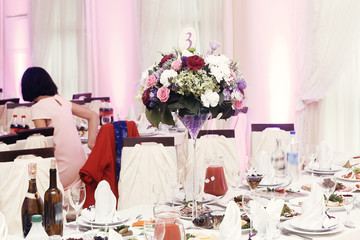 flowers in vases and numbers of setting at wedding tables with food in restaurant, luxury wedding reception, stylish decor and catering. rustic bouquets