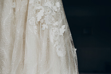 luxury wedding dress detail, hanging on window in a hotel room. modern amazing bride's gown with flowers close-up in light. morning preparation, getting ready. space for text . wedding day