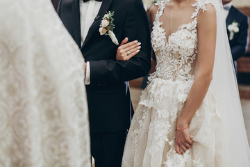 luxury wedding couple hugging, holding hands during traditional wedding ceremony in church. priest...