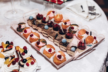 luxury wedding catering, table with modern desserts, cupcakes, sweets with fruits. delicious candy bar at expensive wedding reception. space for text. shower. holiday celebration