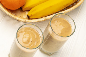 Top view on glasses with banana smoothie and basket with bananas and orange