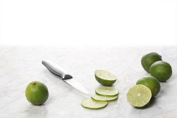 whole and slices lime fruits with a knife on a marble table, white background and copy space for your text