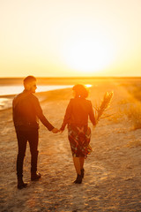 Fototapeta premium Enjoying time together. Stylish and loving couple enjoying each other by the sea. The couple is young and in love. The concept of youth, love and lifestyle. Beautiful sunset on a summer day.