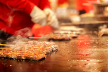 Closeup Kobe beef stick on a hot pan to sale for customer at Kuromon market on blurry hands of chef cooking background. Kobe beef stick Bar-B-Q is most popular among tourists who come to Japan.