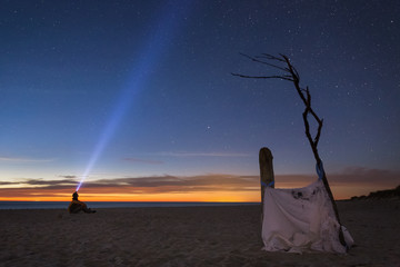 A young man sitting on the sandy beach, relaxing and enjoying the deep night and the starry sky