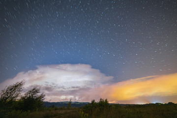 Powerful thunderstorm with lightnings at night with starry sky on the background