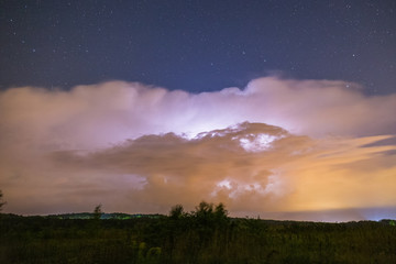 Powerful thunderstorm with lightnings at night with starry sky on the background