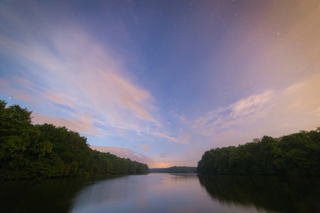 Fototapeta na wymiar Small calm lake at night. Starry and cloudy sky