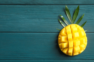 Cut ripe mango and palm leaf on wooden background, space for text