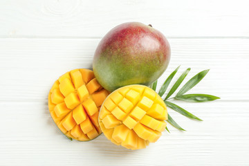 Cut ripe mangoes and palm leaf on white background, space for text