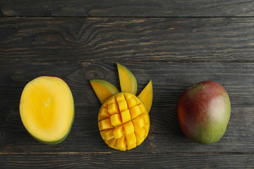 Cut ripe mangoes and space for text on wooden background, top view