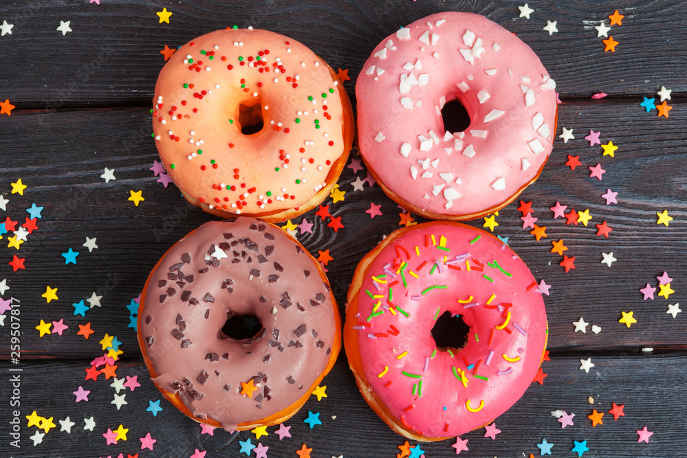 Poster Assortment of colorful donuts decorated with colorful confetti sprinkles on dark wooden background