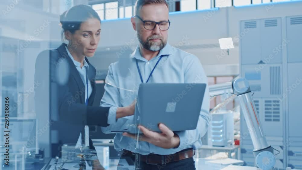 Poster female chief engineer talks with male electronics specialist, explaining things, he holds on laptop 