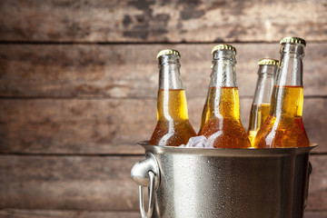 Cold bottles of beer in the bucket on the wooden background - obrazy, fototapety, plakaty