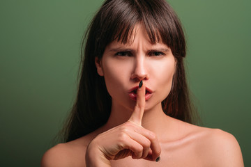 Naklejka premium Outraged lady. Anxious facial expression. Closeup portrait of emotional brunette girl warning with hush gesture. Keep silence.
