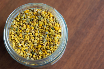 glass vase full of bee pollen granules, seen from above on a dark wooden table.