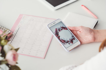 Digital influencer at work. Smartphone in hand. Timetable on desk. Internet marketing. Time frame and growth results.