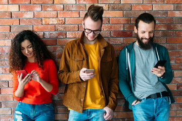 Millennials lifestyle. Group of cheerful young people leaned against wall, using latest...