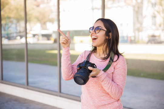 Cheerful woman holding camera and pointing away outdoors