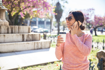 Happy woman drinking coffee and calling on phone outdoors