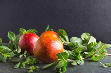 Delicious sicilian oranges and peppermint on the grey table against dark wall.Juicy fruits and plant