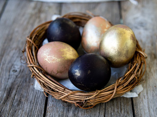 Golden and black eggs in a nest on an old wooden background. Copy space, selective focus, close up. Eggs for Easter. Card.