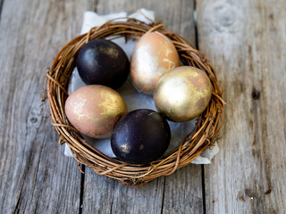 Golden and black eggs in a nest on an old wooden background. Copy space, selective focus, close up. Eggs for Easter. Card.
