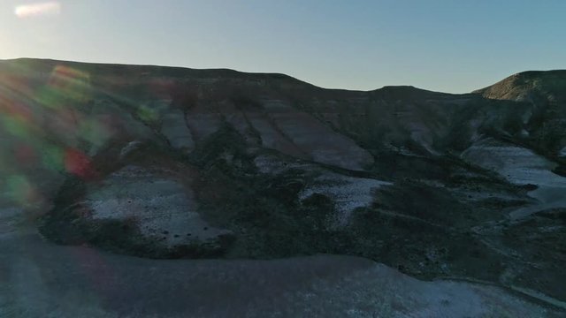 Fast, low aerial view, pulling away from dry, barren mudstone embankments in a desert