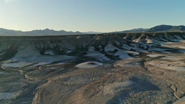 Slow, panning aerial view moving toward dry, barren mudstone embankments in a desert