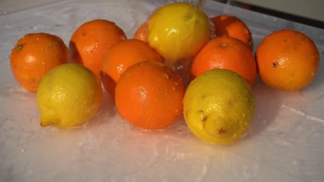 Pouring water over lemons and oranges in slow motion