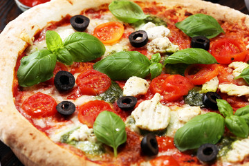 Pizza with tomatoes, mozzarella cheese, black olives and basil. Delicious italian pizza on wooden pizza board.